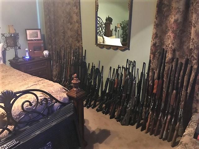 Over 20 guns lined up against a wall.