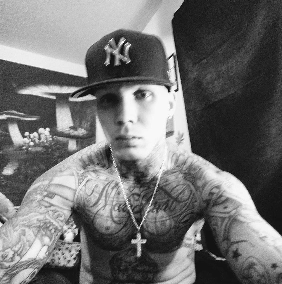 Dillon C. Johnson wearing a hat and no shirt. He has full body tattoos.