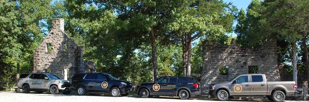 A line of four sheriff vehicles parked next to historic landmarks.