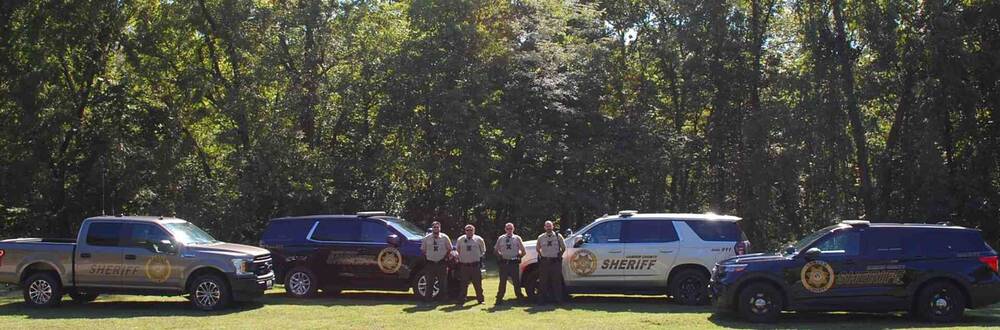 Four deputies standing in front of their sheriff vehicles.